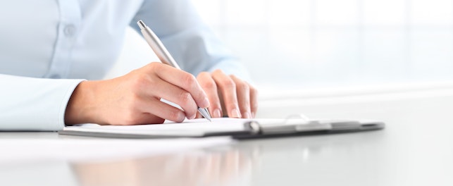 Woman's hands writing on sheet in a clipboard with a pen, isolated on desk